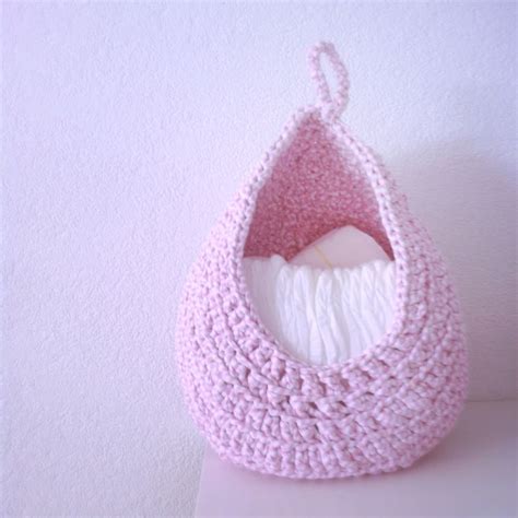 A Pink Crocheted Basket With A White Pillow In The Center On A Table