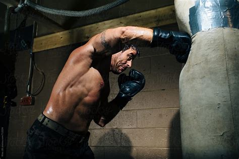 A Boxer Throws A Hard Punch At A Punching Bag In A Gym By Stocksy