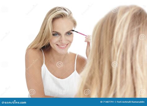 Beautiful Blonde Woman Applying Mascara In Ront Of A Mirror Isolated