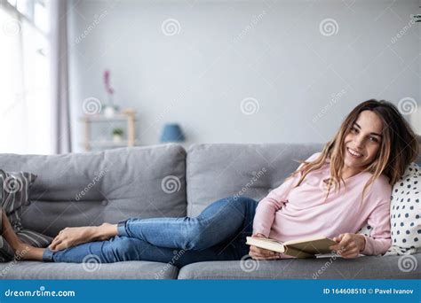 Young Beautiful Woman Is Reading A Book While Lying On A Sofa In The