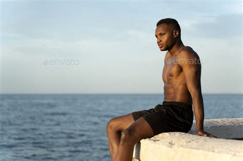 Man With Naked Torso Standing On The Beach And Looking Away While