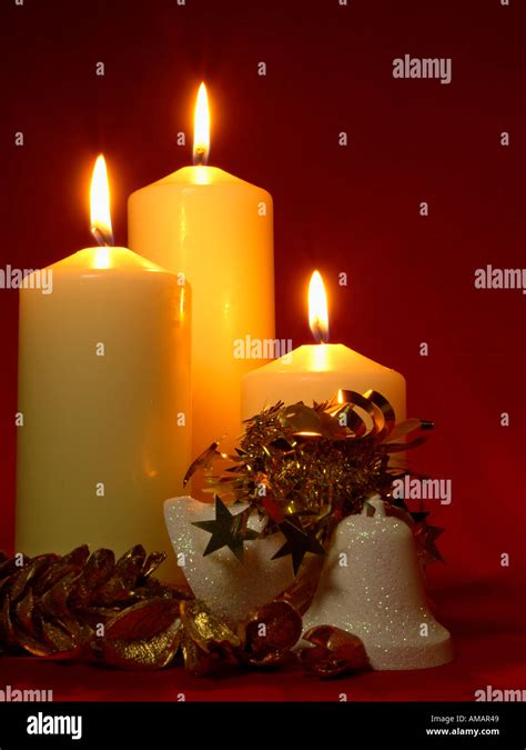 THREE CHURCH CANDLES with Christmas bells and golden fir cones on dark red background Stock ...