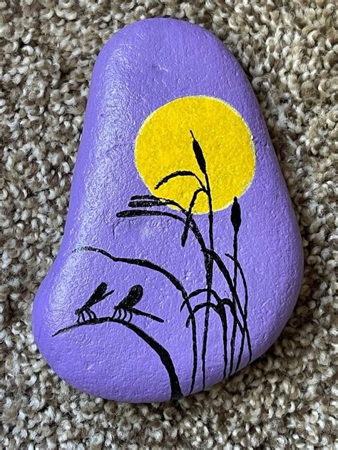 A Painted Rock With Birds On It Sitting On The Ground Next To A