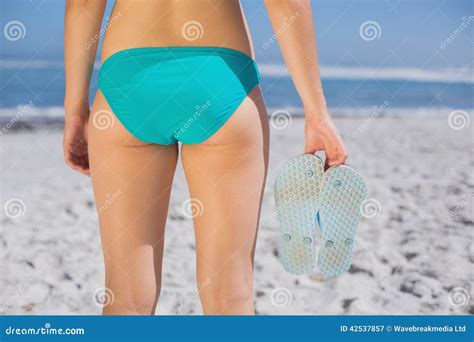 Rear View Of Fit Woman In Bikini On Beach Holding Flip Flops Stock