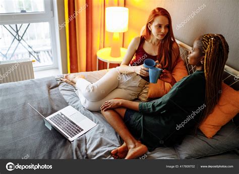 Cheerful Afro And European Lesbian Women At Home On The Bed Stock Photo