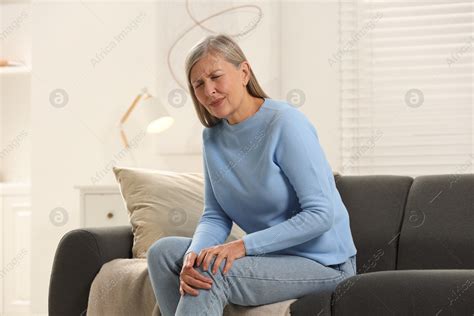 Mature Woman Suffering From Knee Pain On Sofa At Home Rheumatism