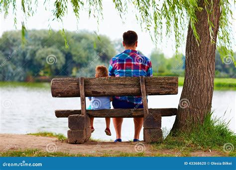 Father And Son Sitting On The Bench Near The Lake Stock Photo Image