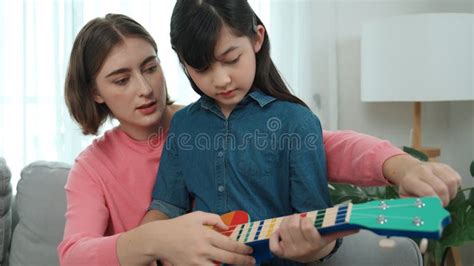 Happy Girl Playing Ukulele While Caucasian Mom Teaching And Explain