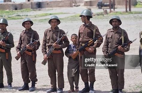 A young Afghan boy stands holding hands with a soldier armed with ...