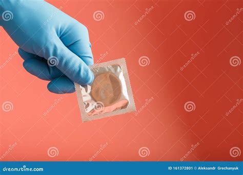 Doctor`s Hand In A Blue Glove Holds A Condom In A Package On A Pink