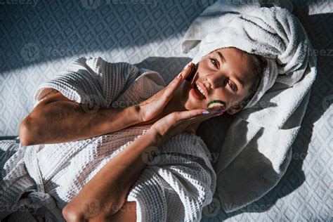 Young Positive Woman With Towel On Head Lying On The Bed With Cucumber