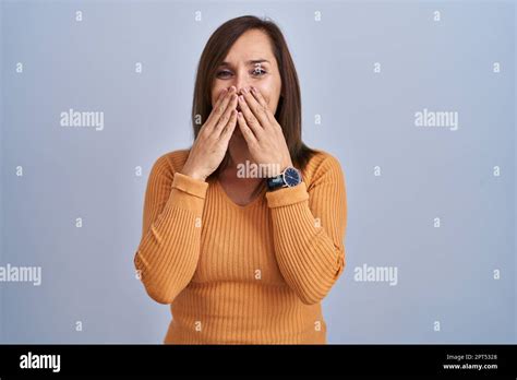 Middle Age Brunette Woman Standing Wearing Orange Sweater Laughing And Embarrassed Giggle