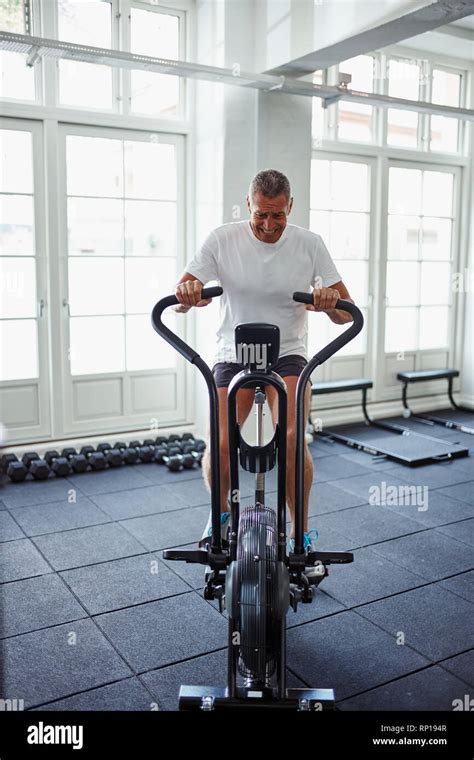 Mature Man In Sportswear Riding A Stationary Bike Pushing Himself To His Limit While Working Out