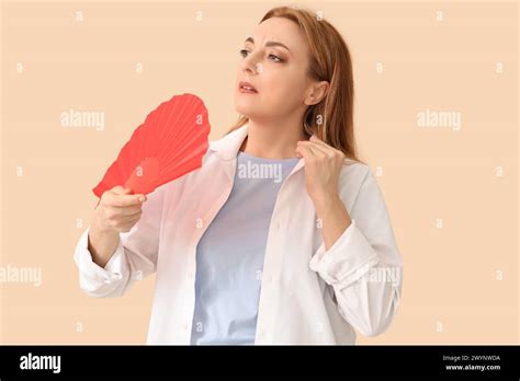 Mature Woman With Fan Suffering From Hot Flashes On Beige Background Menopause Concept Stock