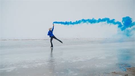 A Caucasian Woman Is Skating On A Frozen Lake Holding Colored Blue