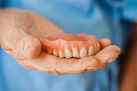 Paciente idosa asiática segurando dentadura de dentes na mão para