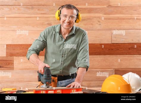 Mature Carpenter Sawing Plank At Table Near Wooden Wall Stock Photo Alamy