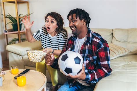 African American Husband And Latina Wife Watching A Football Game On Television From The Comfort