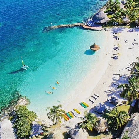 The Beach Is Surrounded By Palm Trees And Clear Blue Water With Boats