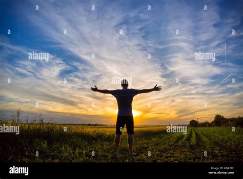 Man Standing In An Open Field At Sunset With Open Arms Embracing