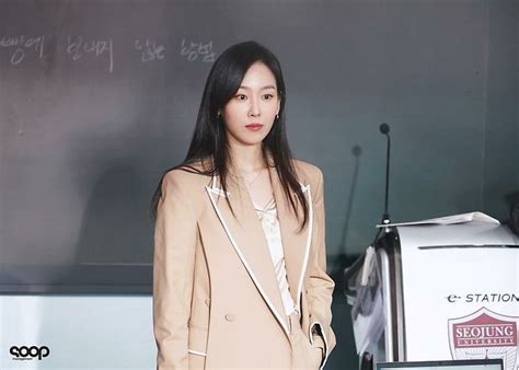 a woman standing in front of a blackboard wearing a tan suit and white ...