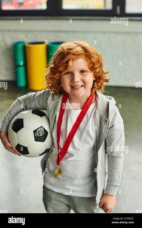 Vertical Shot Of Pretty Red Haired Boy With Golden Medal Holding Soccer