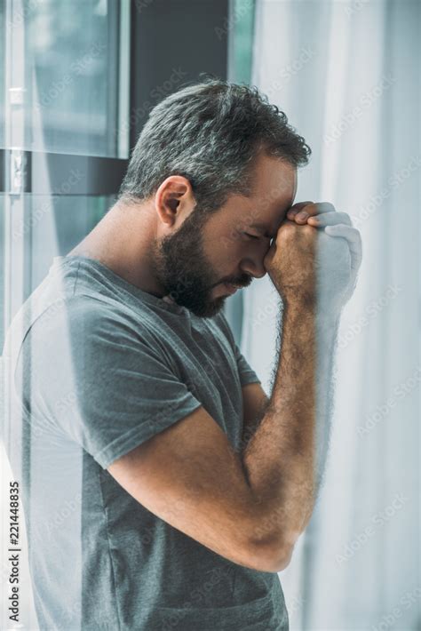 Side View Of Depressed Frustrated Bearded Man Standing Near Window