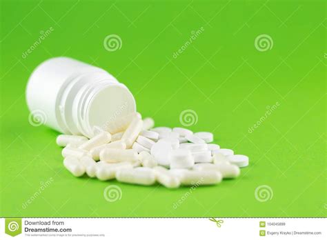 Close Up White Pill Bottle with Spilled Out Pills and Capsules on Green ...