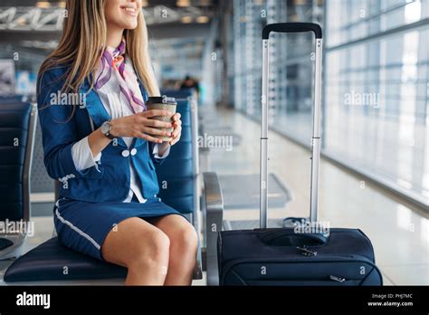 Stewardess With Coffee And Suitcase Sitting On Seat In Waiting Area In