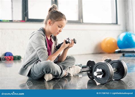 Niña Linda Que Se Sienta En Piso Y Que Ejercita Con Pesas De Gimnasia