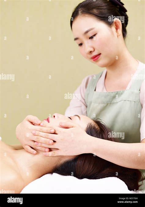 Young Asian Masseur Performing Face Massage On Woman In Spa Salon Stock