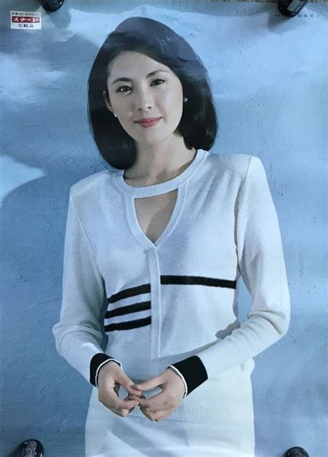 A Woman Standing In Front Of A Blue Background Wearing A White Sweater