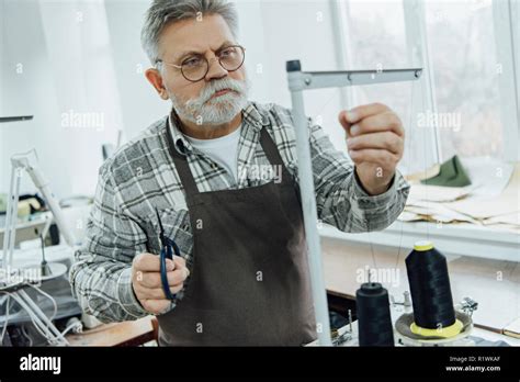 Focused Mature Male Tailor In Apron Setting Strings On Sewing Machine