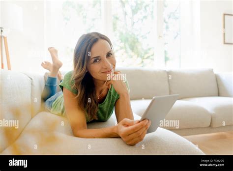 Portrait Smiling Mature Woman Lying Couch Home Using Tablet Hi Res