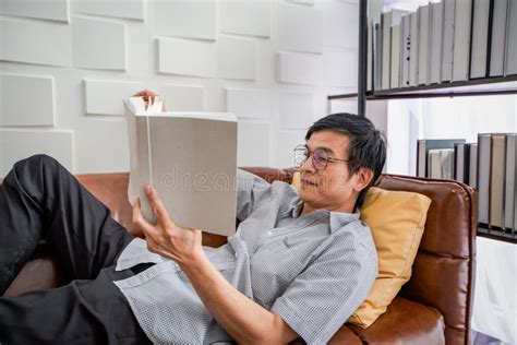 Senior Asian Man Reading Book On Sofa In Living Room At Home Portrait Of Asian Elderly Man Is