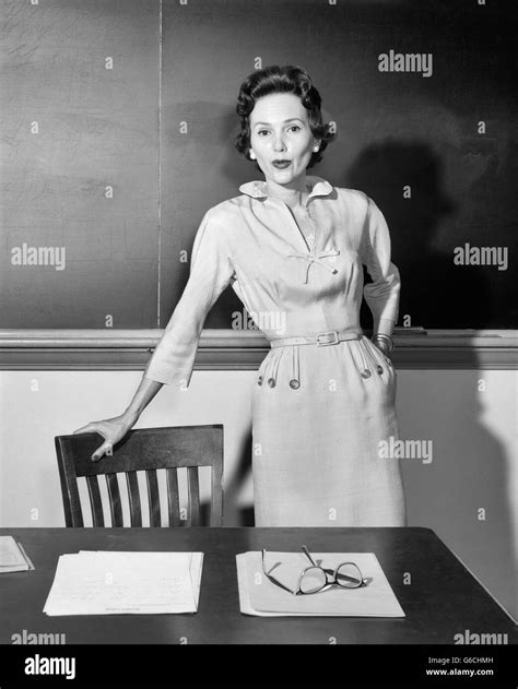 1950s Woman School Teacher Looking At Camera Standing In Front Of Chalkboard In Classroom