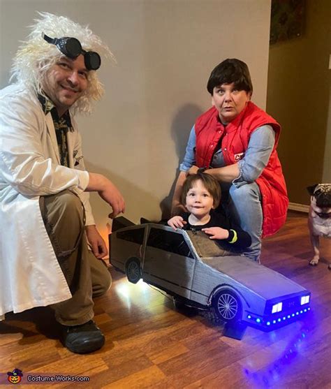 two adults and a child sitting on top of a toy car in front of a dog