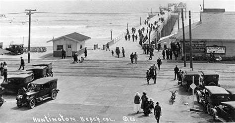 An Old Black And White Photo Of People Walking On The Beach With Cars