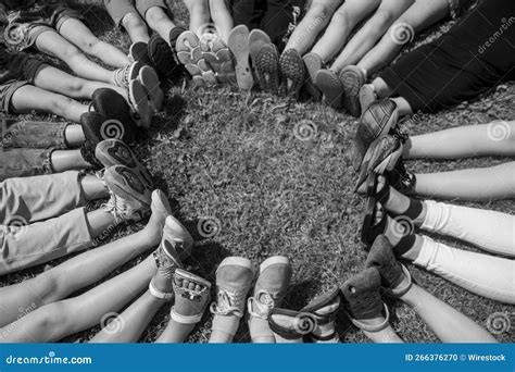 Grayscale Shot Of People Forming A Circle With Their Feet In A Field