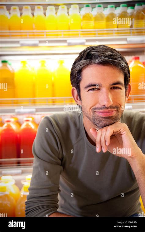 Portrait Of Smiling Man Sitting In Front Of Fridge With Rows Of Juice