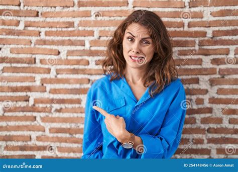 Beautiful Brunette Woman Standing Over Bricks Wall Pointing Aside Worried And Nervous With