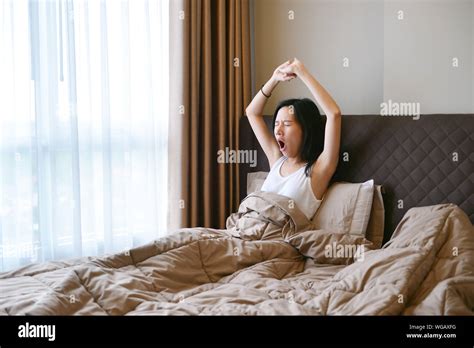 Young Woman Yawning While Sitting On Bed At Home Stock Photo Alamy