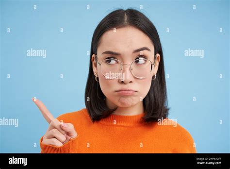 Portrait Of Japanese Woman In Glasses Points Left Looks Aside At Banner Stands Over Blue