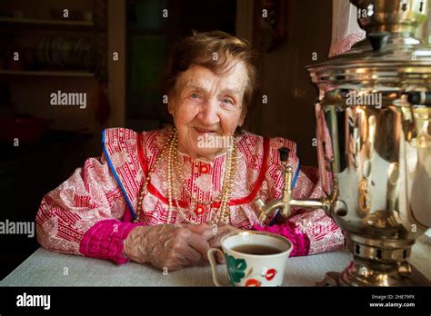 An Elderly Woman In Russian National Dress Is Sitting Drinking Tea With