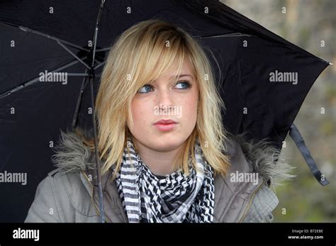 Blonde 18 Year Old Girl Holding Black Umbrella Wearing Jacket And Heavy Scarf Looking Away From