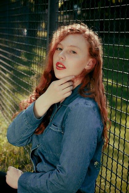 Premium Photo Attractive Redhead Young Model Sitting Near Fence In Rays Of Sun