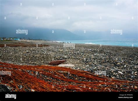 Red Fishing Net On Shingle Beach With Pacific Ocean And Mountains In