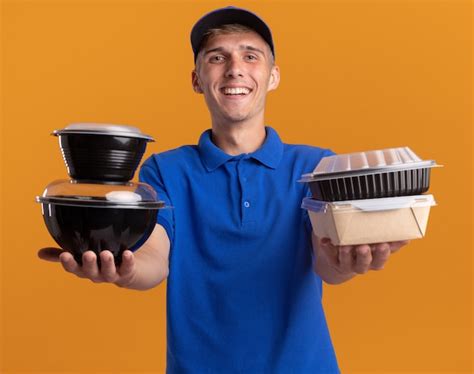 Souriant jeune livreur blonde détient des contenants de nourriture sur orange Photo Gratuite