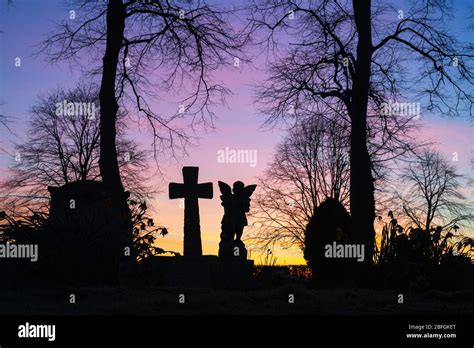 Silhouette of an angel and cross headstone with trees in a cemetery at ...