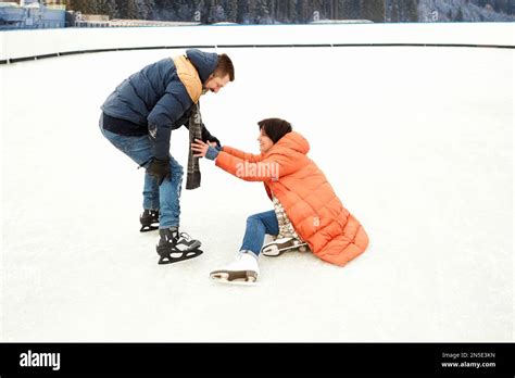 Middle Aged Couple Skating On Open Air Ice Rink Man Helping Fallen